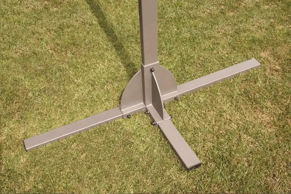 Pied d’un abri de terrasse posé sur une pelouse, sa platine en croix et le départ du mât