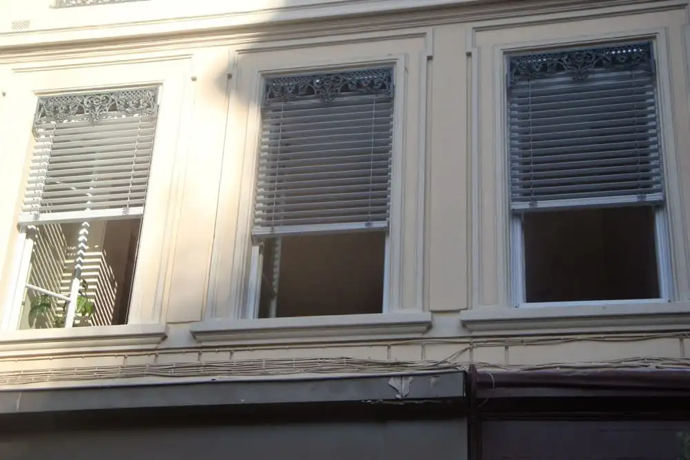 Façade d’immeuble lyonnais : brise-soleil orientables gris clair derrière les cantonnières en fonte des fenêtres