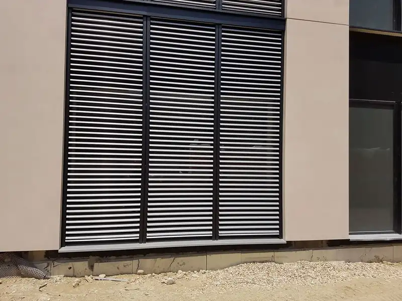 Brise-soleil orientables baissés devant une baie : lames horizontales en aluminium