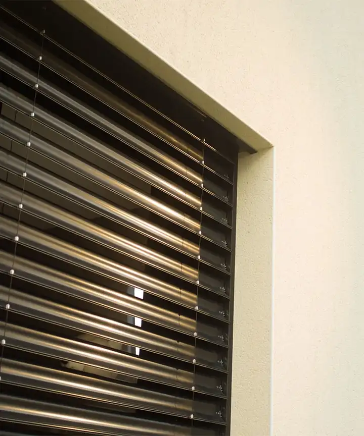 Gros plan sur les lames en aluminium d’un brise-soleil orientable, à demi inclinées devant une baie