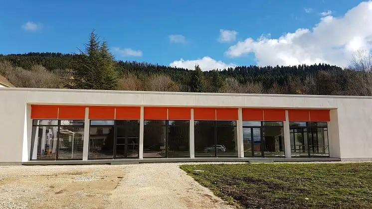 Bâtiment de plain-pied de l’hôpital de Hauteville-Lompnes, stores enrouleurs orange à demi déroulés devant les baies