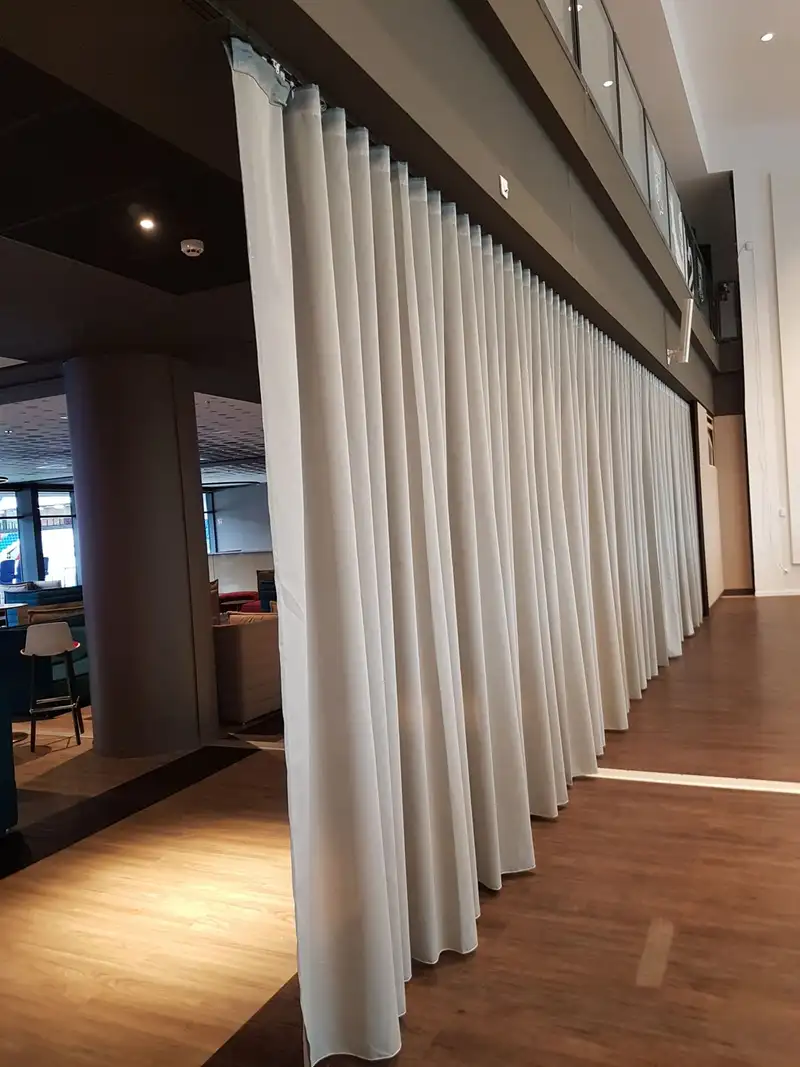 Rideau blanc à plis réguliers, tombant du plafond jusqu’au parquet