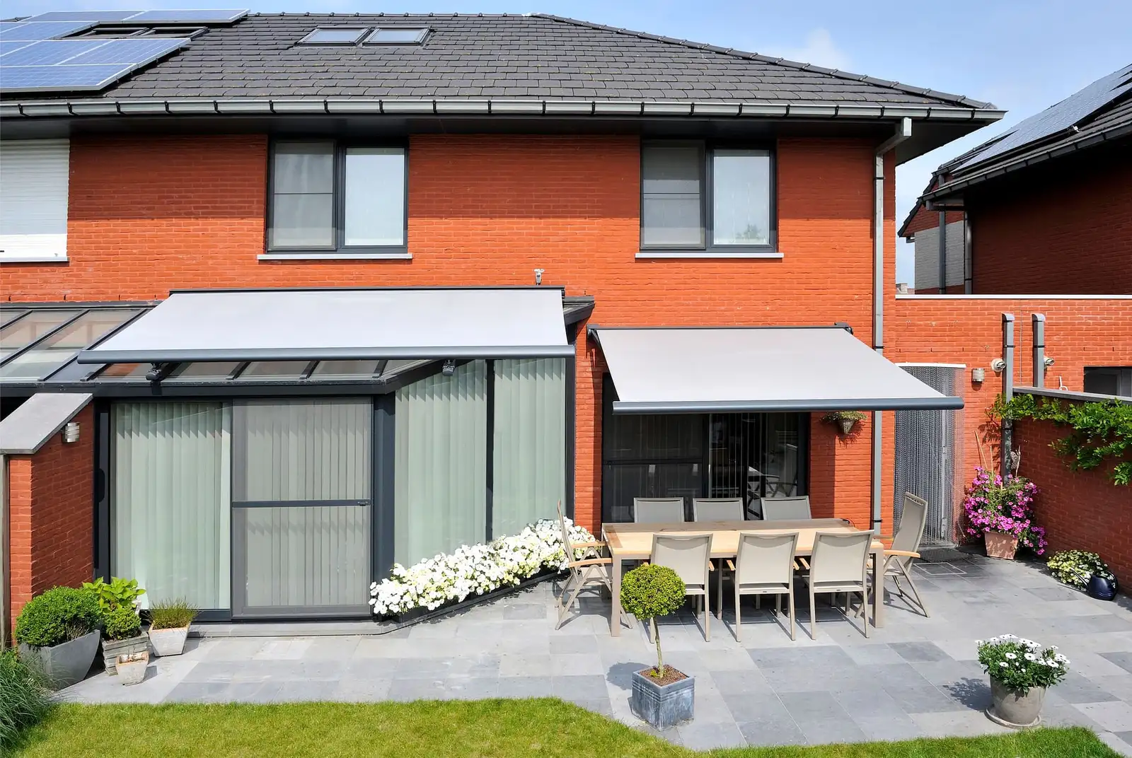 Maison de brique dont la véranda est couverte par un store de toiture et la terrasse par un store banne