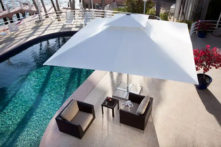 Parasol carré à toile blanche au-dessus d’un salon de jardin, au bord d’une piscine