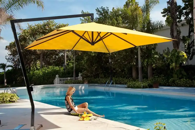 Parasol déporté à toile jaune au-dessus du bord d’une piscine, son mât posé sur le côté