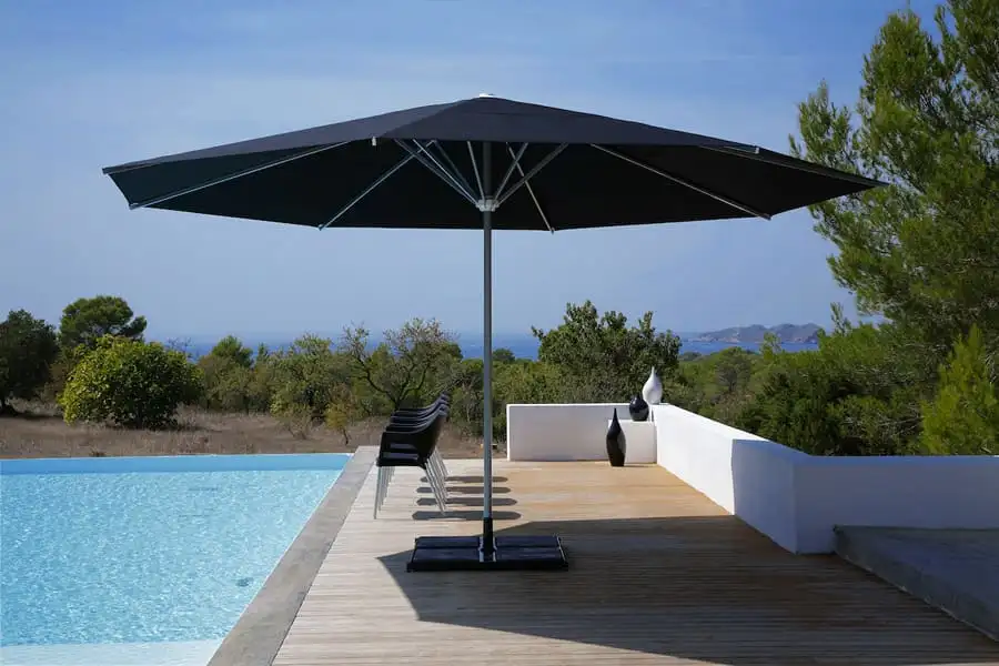 Grand parasol à toile sombre sur une terrasse en bois, au bord d’une piscine à débordement