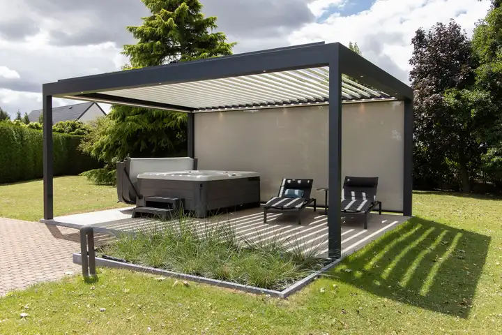 Pergola à lames autoportée sur une pelouse, un spa et deux transats à l’abri, un screen fermant le fond