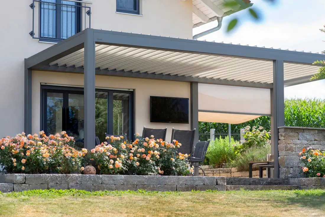 Pergola grise à lames adossée à une maison crépie, devant ses baies, un screen déroulé sur le côté