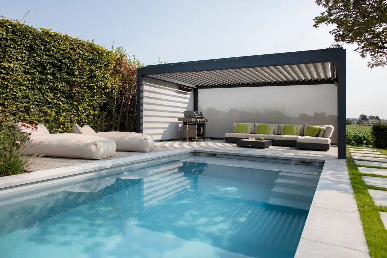 Pergola bioclimatique anthracite à lames orientables au bord d’une piscine, devant une haie