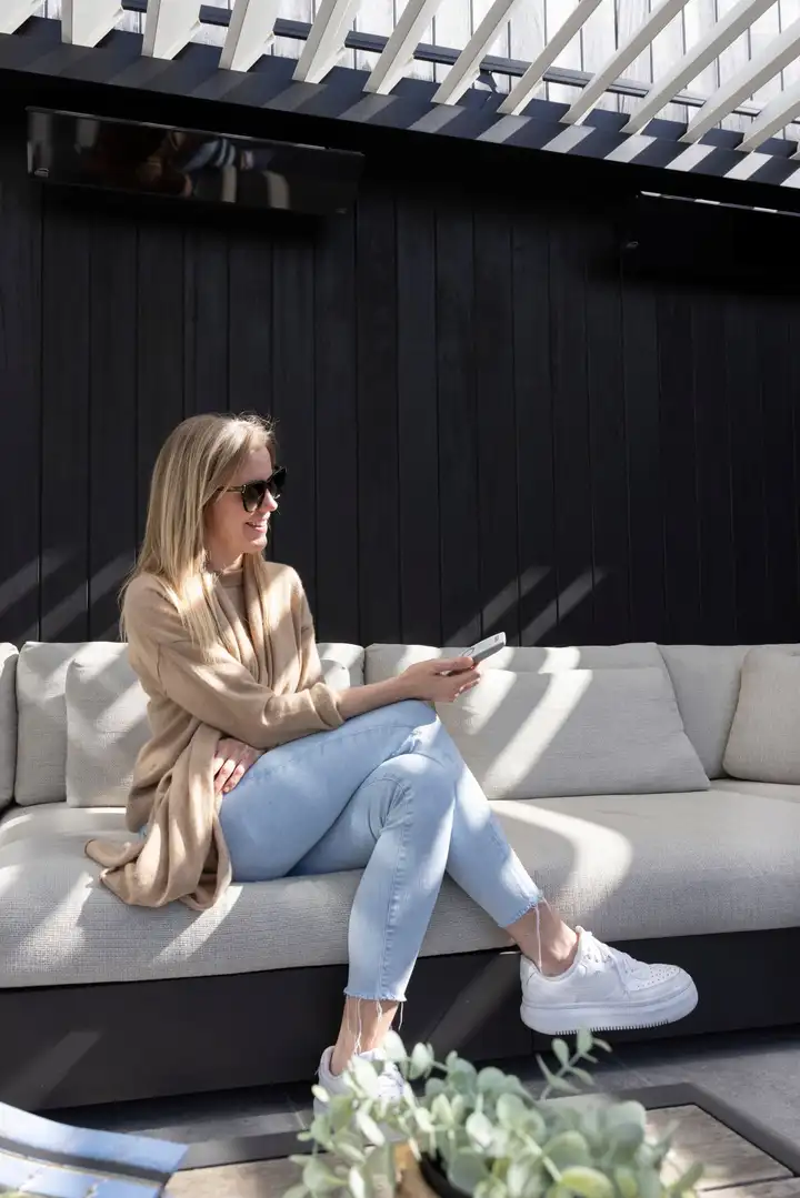 Une femme assise sous une pergola règle les lames depuis son téléphone