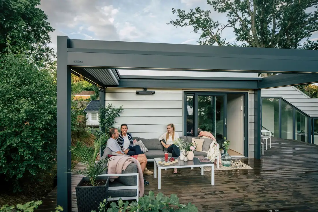 Trois amis sur une terrasse en bois, sous une pergola à toile adossée à une maison blanche
