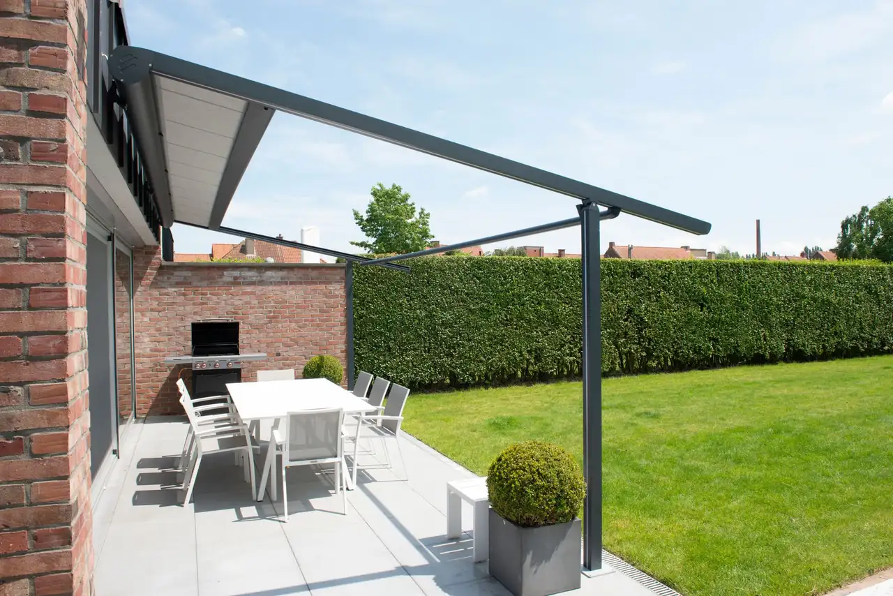 Pergola à toile rétractable adossée à une maison en brique, au-dessus d’une terrasse et de sa table