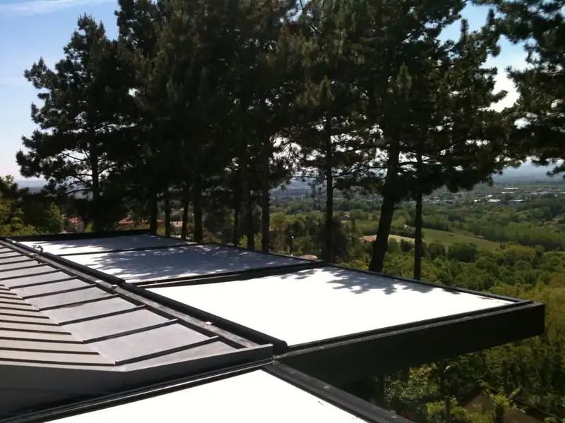 Toiles blanches rétractables d’une pergola, au-dessus d’une terrasse qui domine la campagne lyonnaise