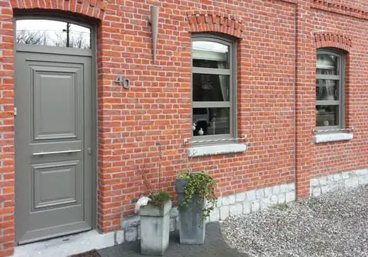 Porte d’entrée grise à panneaux moulurés dans une façade en brique, près de fenêtres de la même teinte