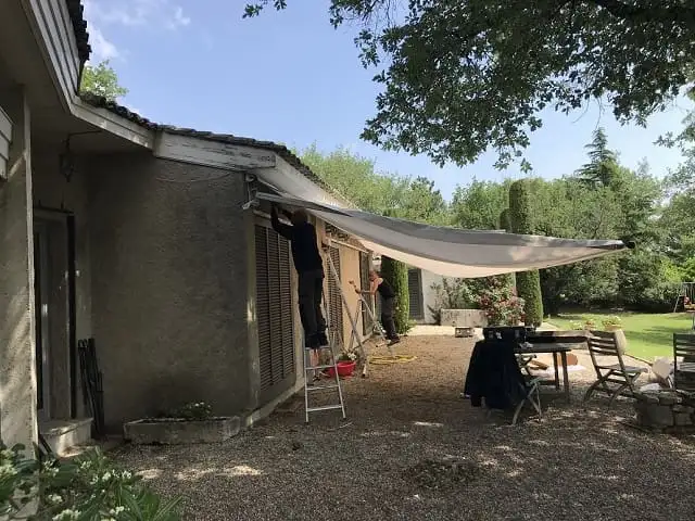 Deux techniciens fixent la nouvelle toile sur l’armature, contre la façade