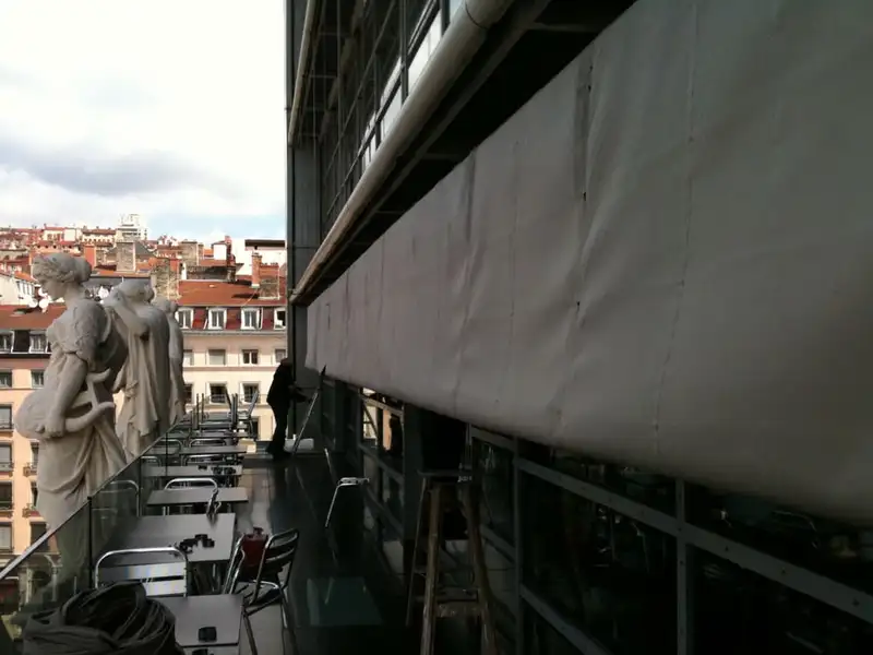 Le long store de la terrasse des Muses, face aux statues et aux toits de Lyon