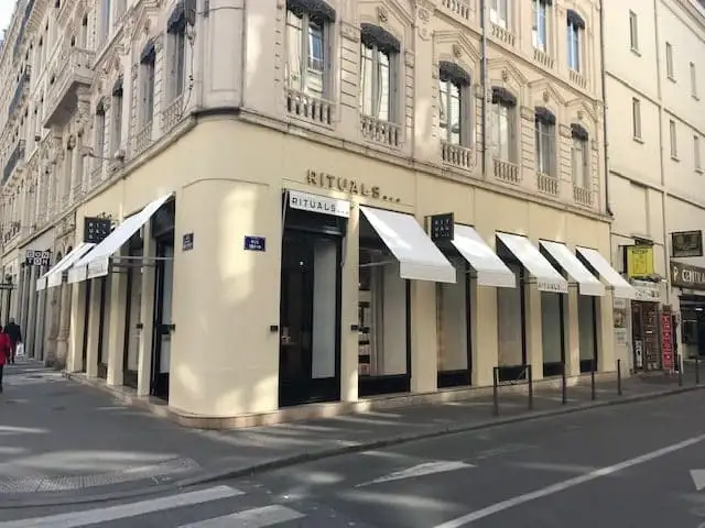 Angle d’un immeuble lyonnais dont les vitrines Rituals sont abritées par des bannettes blanches