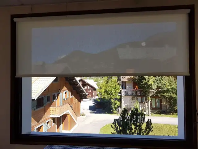 Store enrouleur à toile screen à demi baissé devant une fenêtre donnant sur des chalets