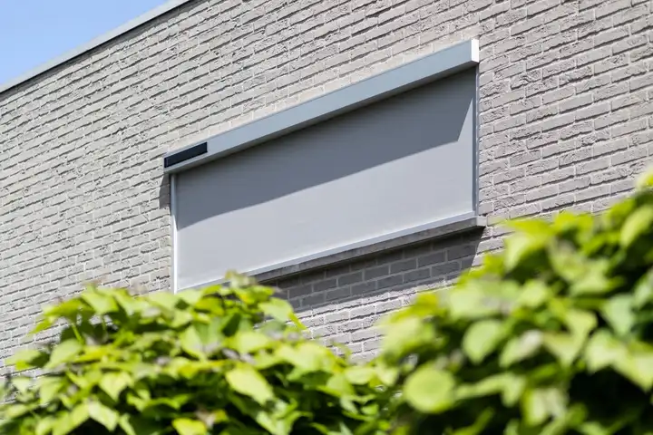 Store enrouleur extérieur posé en applique sur un mur de brique, un petit panneau solaire sur son coffre