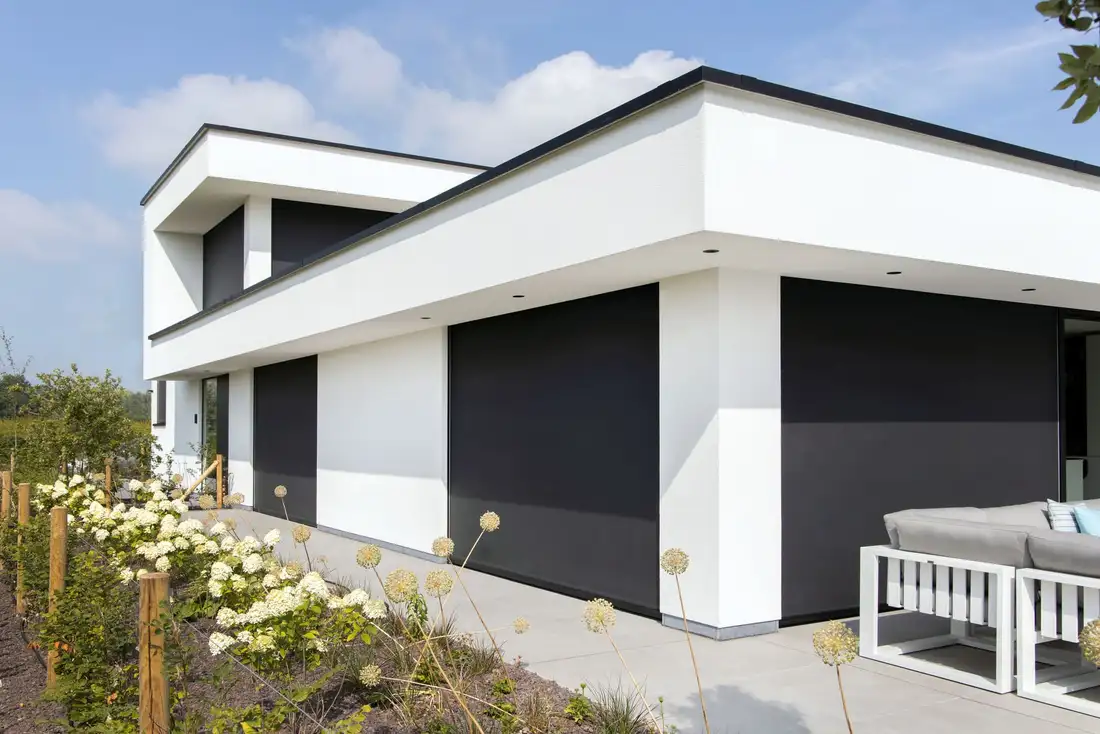 Maison contemporaine blanche dont les baies sont fermées par des stores enrouleurs extérieurs sombres encastrés dans la façade