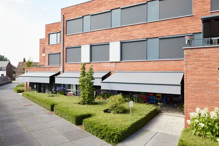 Immeuble de brique dont les fenêtres sont équipées de stores enrouleurs extérieurs gris, stores à projection au rez-de-chaussée