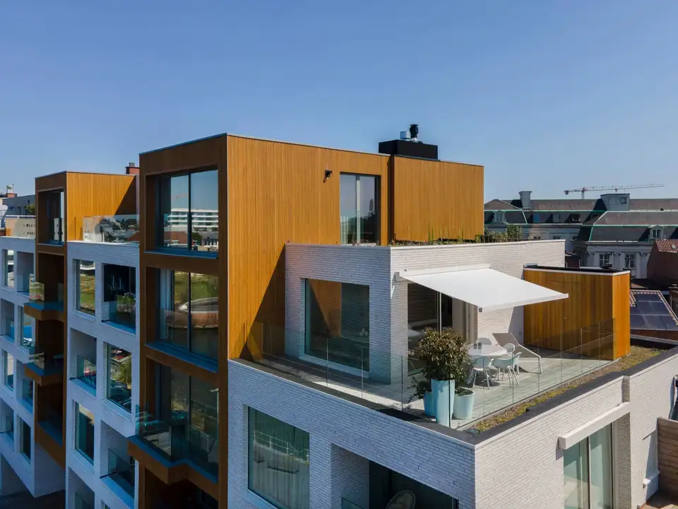 Immeuble contemporain en brique claire et bardage bois : un store banne blanc abrite la terrasse du dernier étage