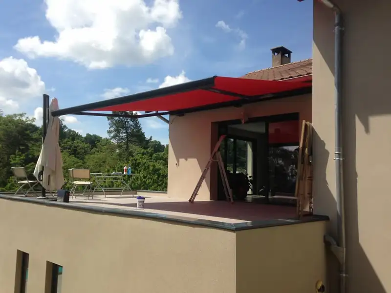 Le store rouge déployé sur toute la largeur du toit-terrasse, au-dessus du salon de jardin