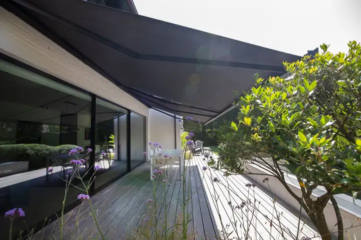 Store banne à armature anthracite et toile sombre au-dessus d’une terrasse en bois