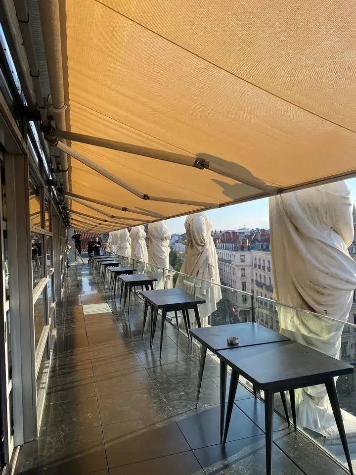 Terrasse de l’Opéra de Lyon sous son store banne, entre les statues du toit