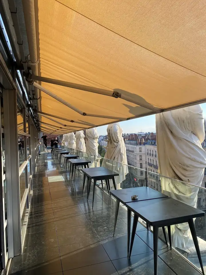 Terrasse de l’Opéra de Lyon sous son long store banne, entre les statues du toit