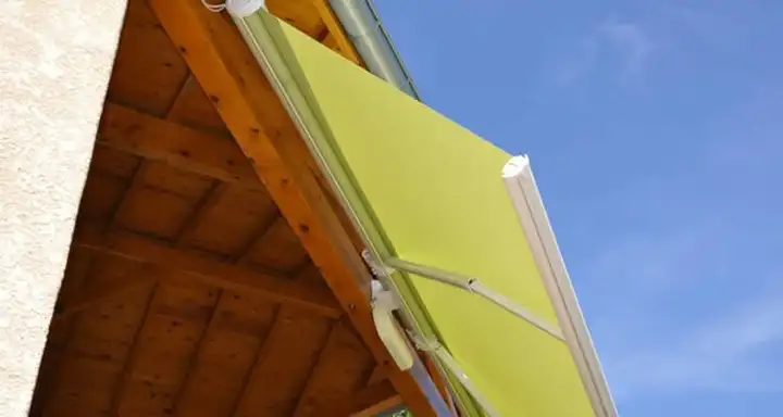 Store inclinable à toile vert anis, orienté vers le bas sous un avant-toit en bois