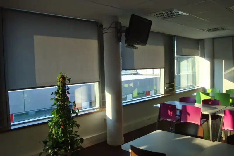 Espace de pause des bureaux du Progrès : stores enrouleurs gris baissés à mi-hauteur devant les fenêtres